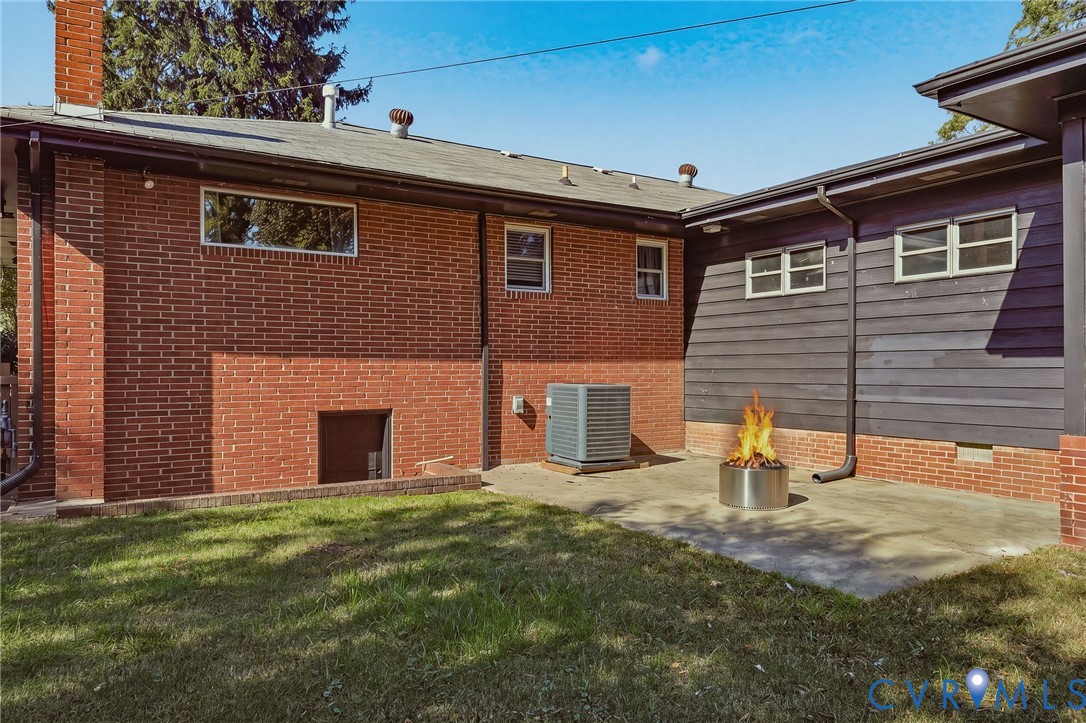 Exterior rear facade featuring red brick and dark horizontal siding, concrete patio, and lawn area