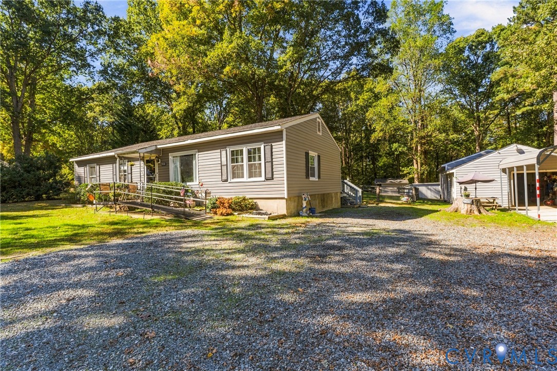 Single-story home featuring horizontal vinyl siding, a gravel driveway, a metal carport, and mature perimeter trees