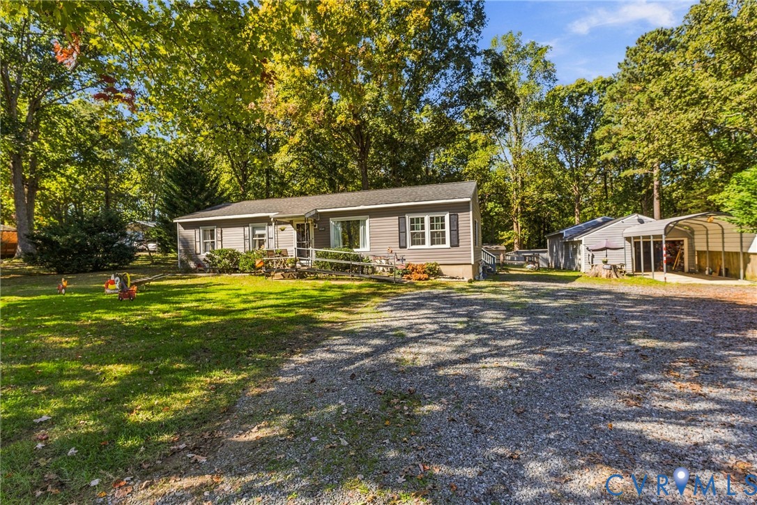 Single-story residence with horizontal siding, multi-pane windows, decorative shutters, a gravel driveway, and a detached carport