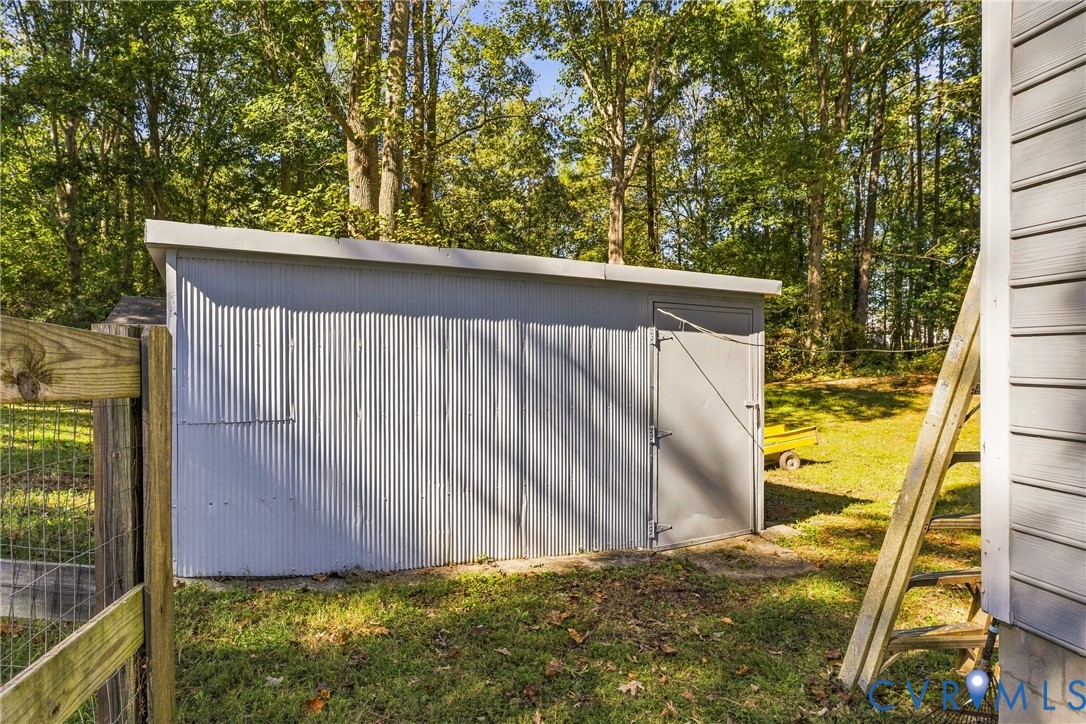 Exterior storage shed featuring corrugated metal siding, a flat roofline, and a solid swing door, situated on a grass lot with mature perimeter trees