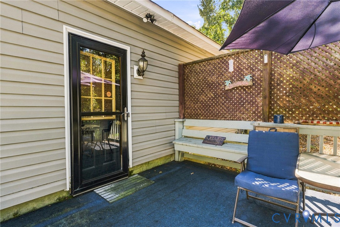 Exterior patio featuring light-toned horizontal siding, a full-lite glass door with paneled glazing, a built-in bench, and wood lattice privacy screening