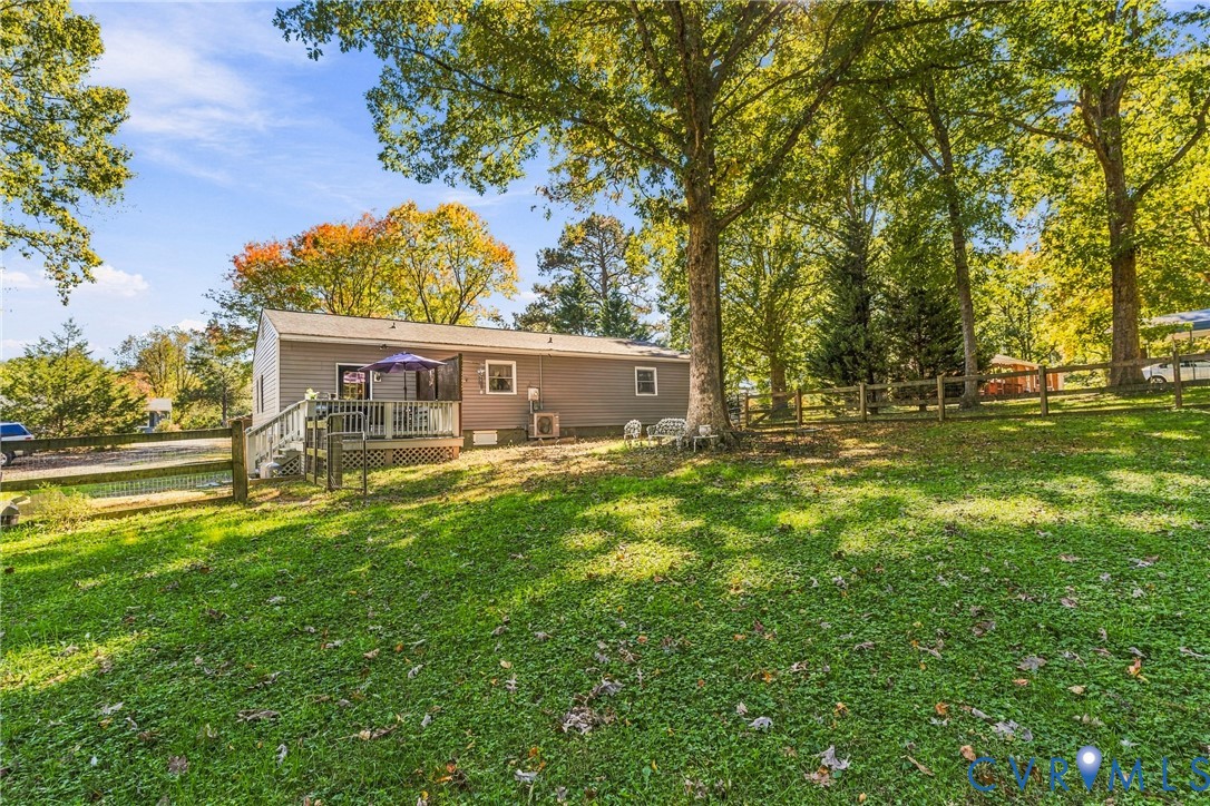Exterior rear elevation featuring horizontal siding, a raised wooden deck with railings, and a fenced yard with mature trees