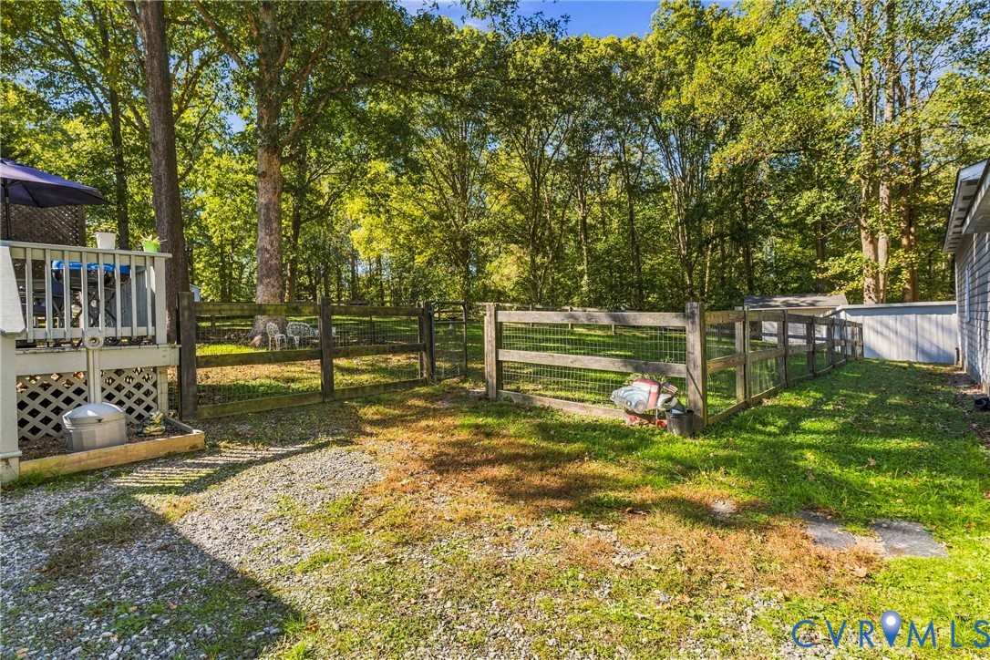 Rear exterior featuring a wood deck, gravel hardscaping, split-rail fencing with wire mesh, and mature perimeter trees