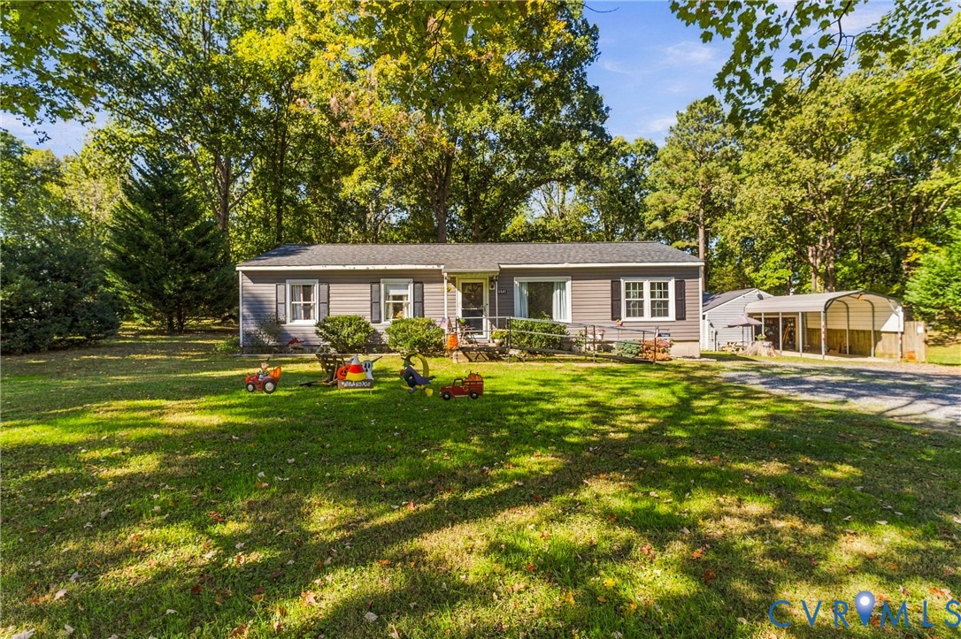 Single-story residence with horizontal siding, a gabled roof, multi-pane windows, and an attached metal-frame carport situated on a partially wooded lot