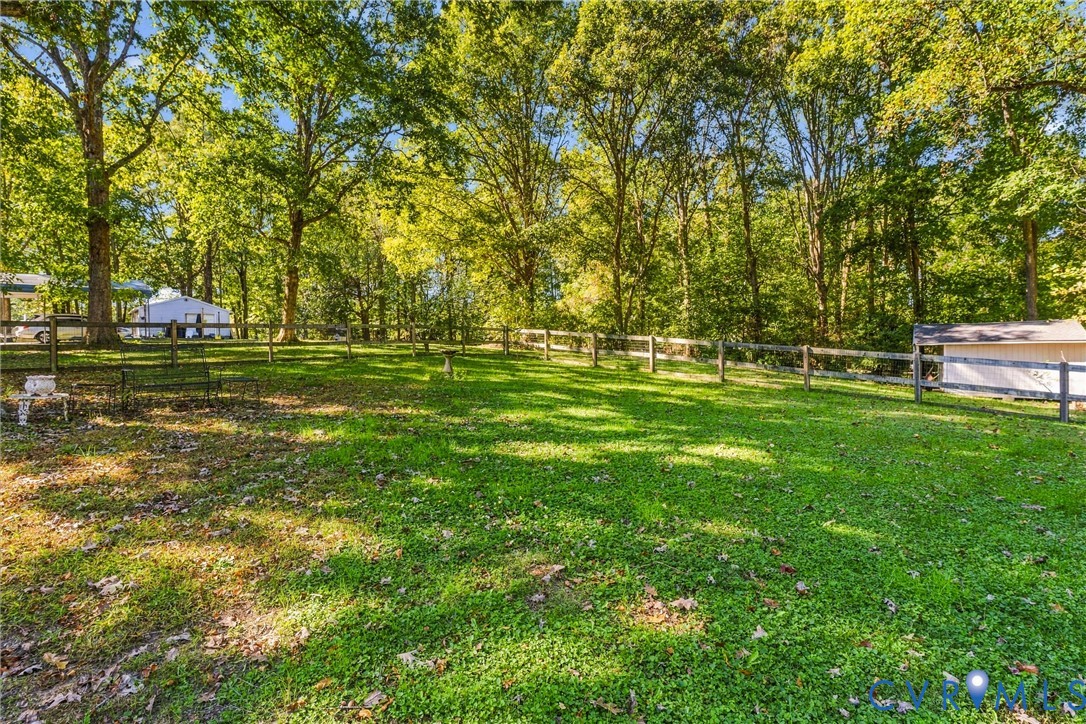 Expansive backyard featuring a post-and-rail perimeter fence, mature trees, and a grass lawn