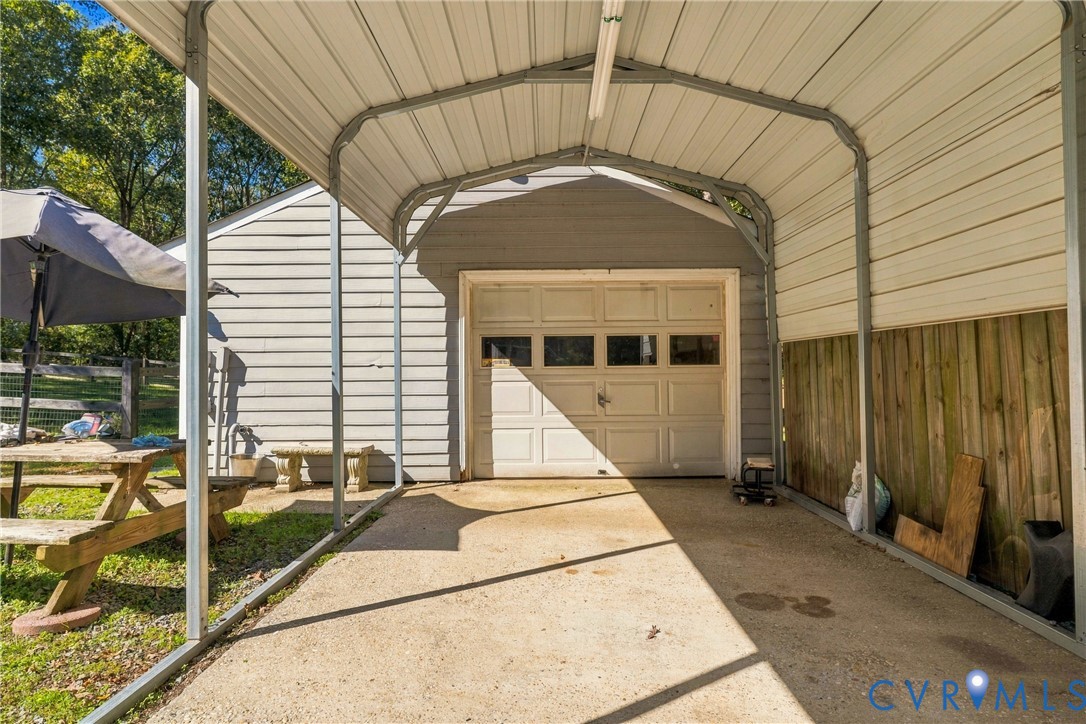 Metal-framed carport featuring a concrete parking pad, attached to a garage with a multi-panel sectional door and horizontal siding