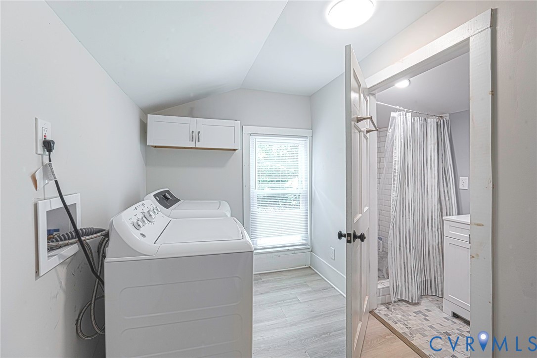 Utility room featuring wood-finish flooring, white wall-mounted cabinetry, a window, and an entry to a bathroom equipped with a shower and vanity