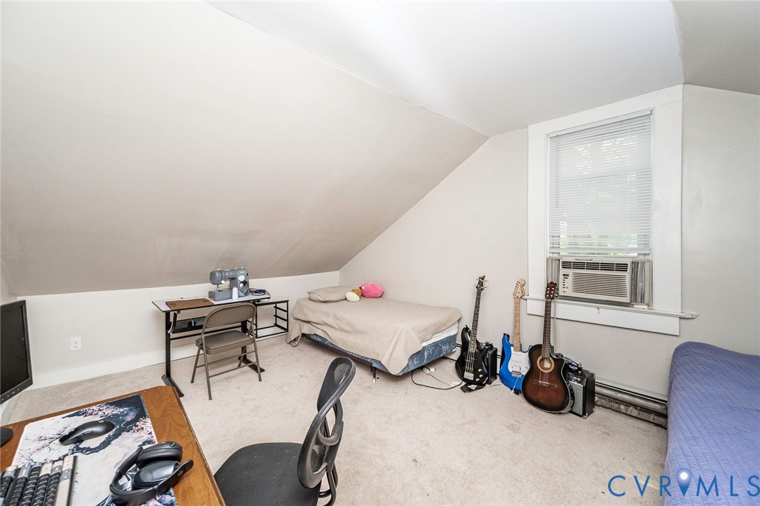 Sloped ceiling, neutral wall tones, wall-to-wall carpeting, and a window with a fitted air conditioning unit
