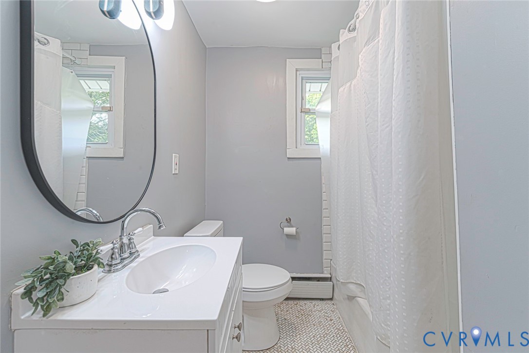 Bathroom featuring a white vanity with an integrated sink, polished chrome faucet, oval wall mirror, and tub-shower combination with white tile surround