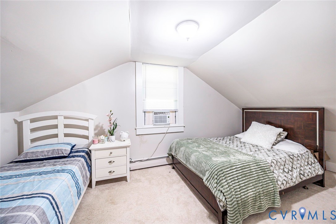 Vaulted ceiling with neutral wall finish, wall-to-wall carpeting, and a centrally positioned window with white trim