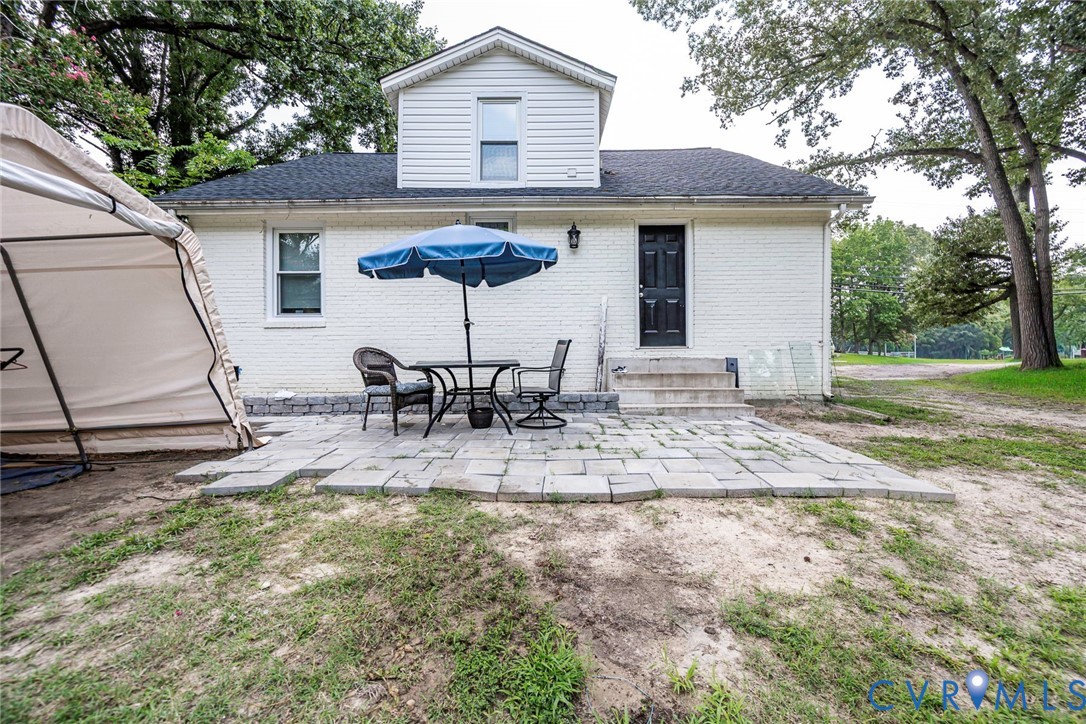 Exterior featuring white brick siding, a stone paver patio, dormer window, and an attached entry with concrete steps