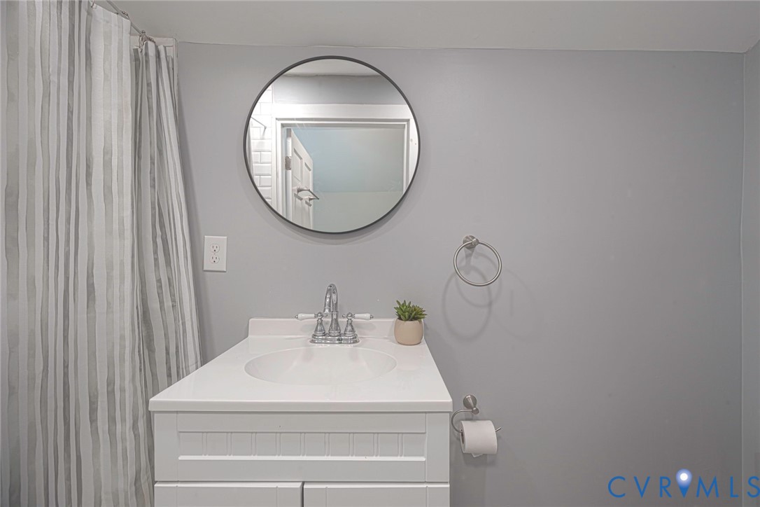 White vanity with an integrated countertop, circular mirror, metallic dual-handle faucet, and hardware accessories