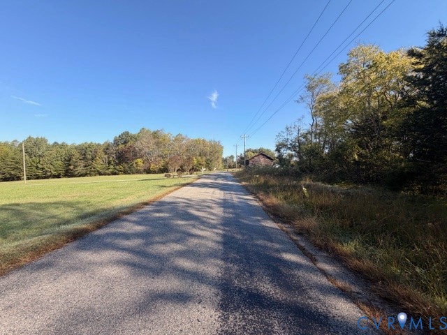 Asphalt road frontage bordered by open pasture, mature trees, and dense foliage Asphalt road frontage bordered by open pasture, mature trees, and dense foliage
