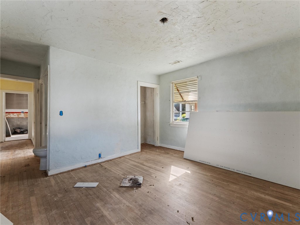 Interior space featuring wood-finish flooring, a single-hung window with metal awning, and neutral wall surfaces