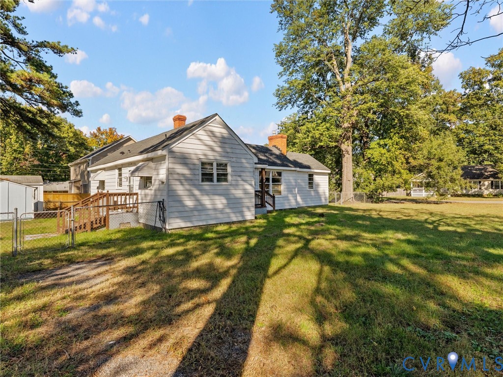 Exterior featuring light-toned horizontal siding, two brick chimneys, an elevated wooden deck, and a spacious lot with mature trees