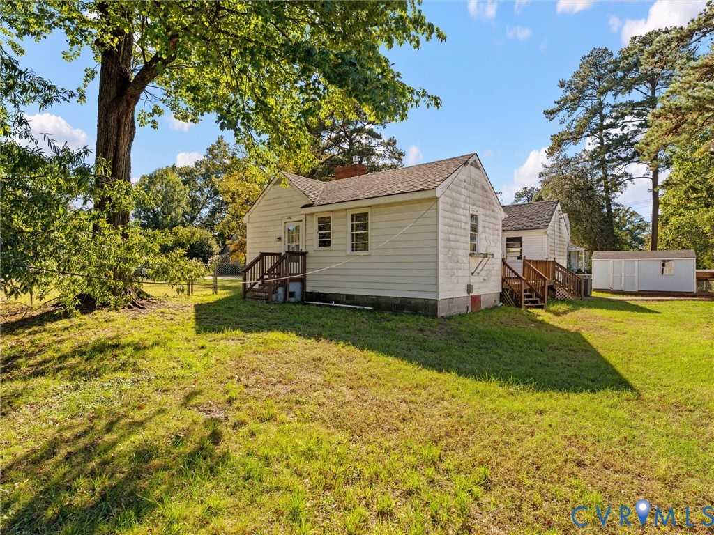 Single-story residence featuring light-colored horizontal siding, dual wood-frame exterior staircases, a brick chimney, and a detached storage structure on a spacious lot with mature trees