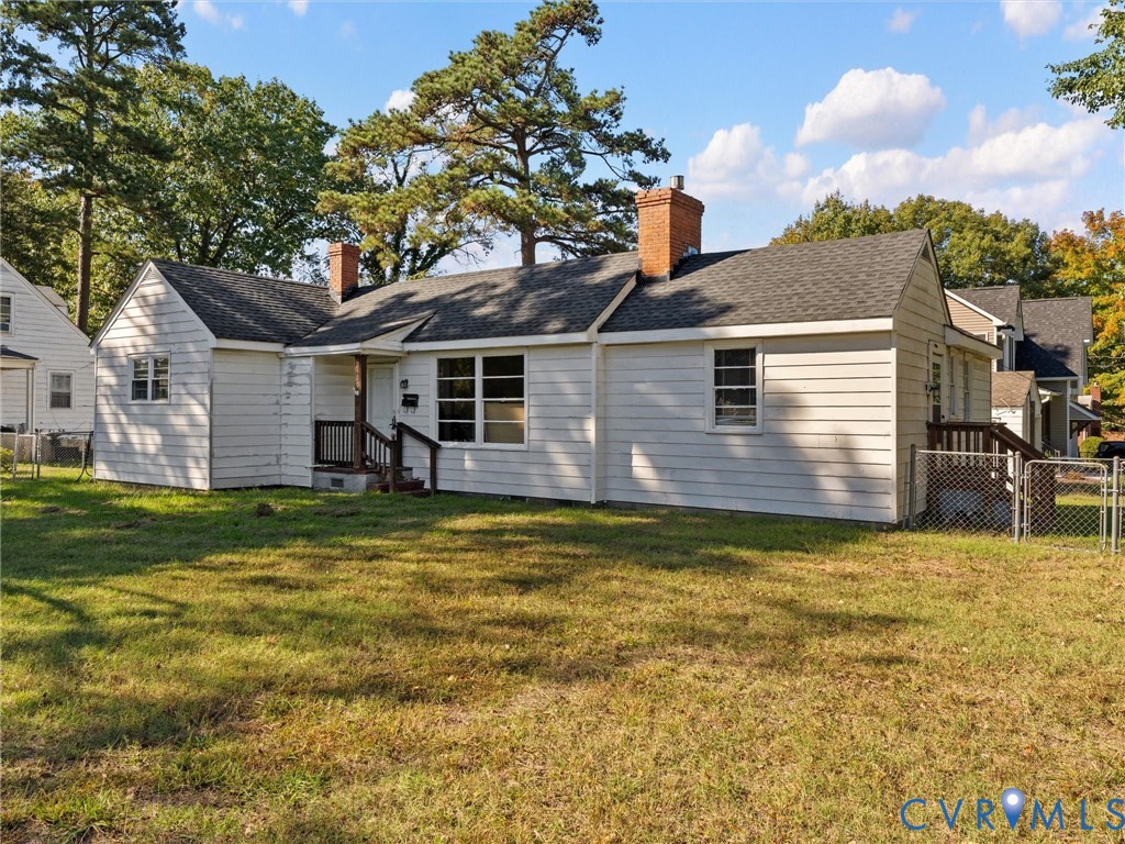 Single-story exterior featuring white horizontal siding, two brick chimneys, a shingled roof, and a fenced perimeter
