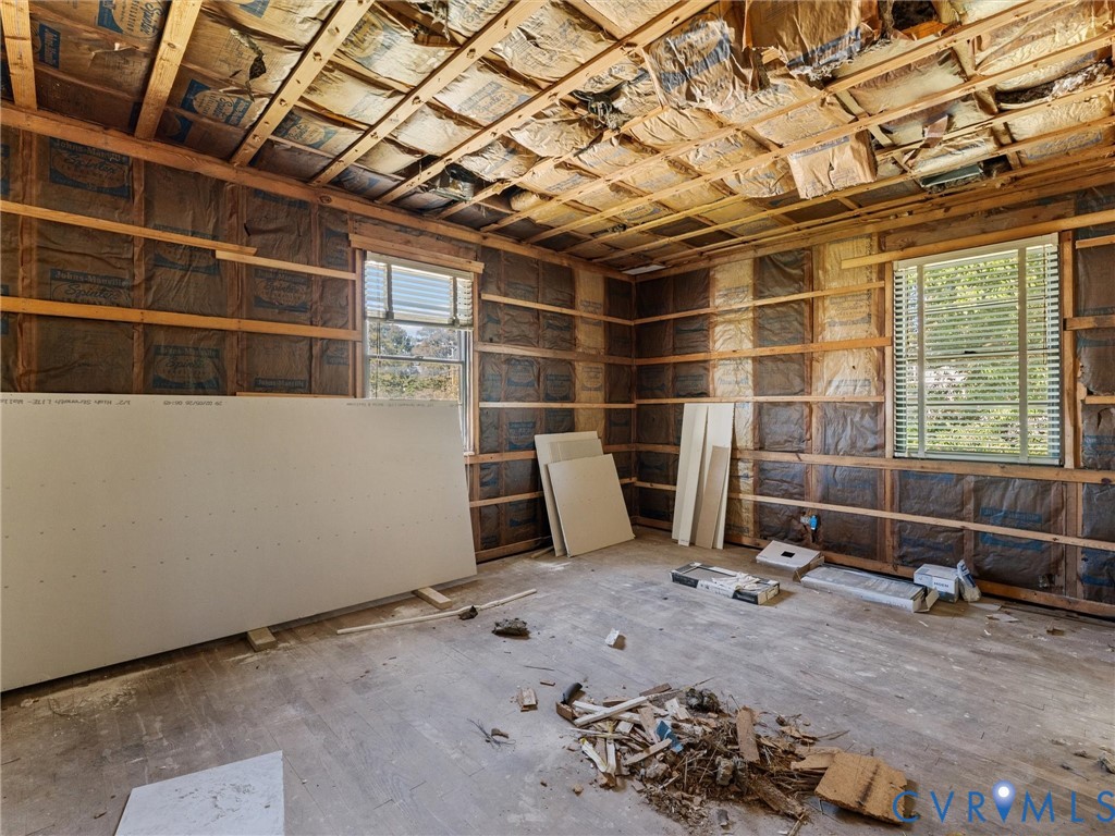 Interior space featuring exposed wood framing, batt insulation, two windows with horizontal blinds, and drywall panels