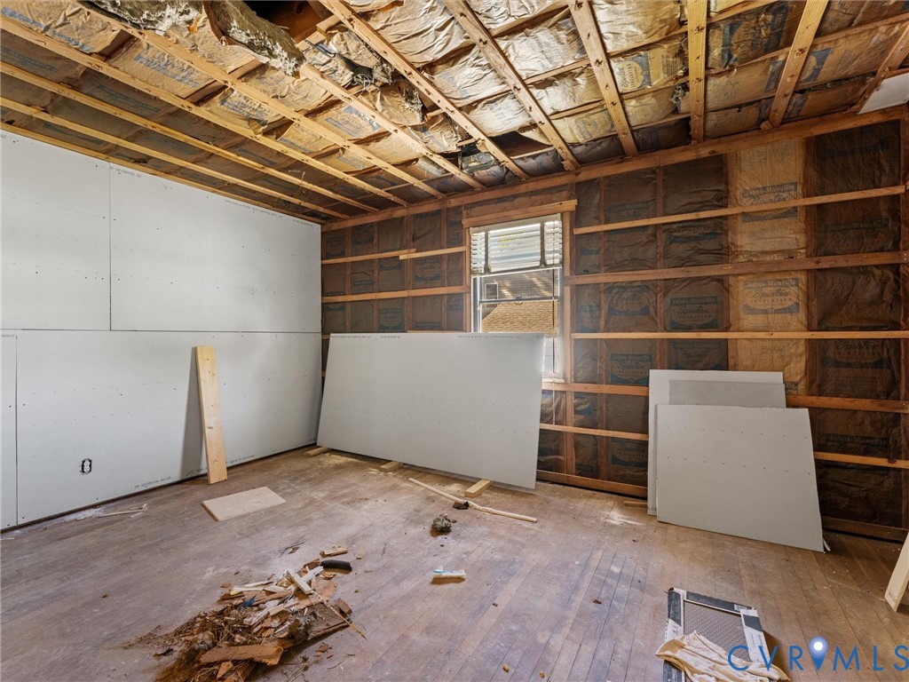 Interior space featuring exposed wood-stud wall framing, partial drywall installation, exposed ceiling joists with insulation, and original wood-finish flooring