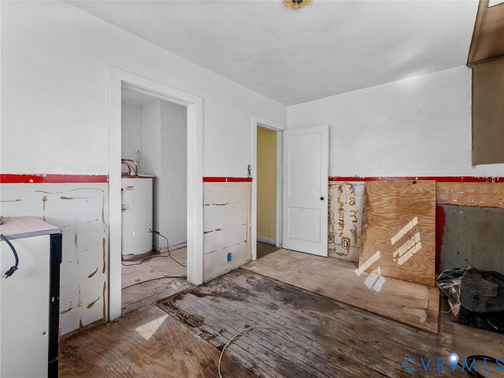 Interior space featuring exposed wood subflooring, partially paneled walls, a single-panel interior door, and a dedicated utility area containing a water heater