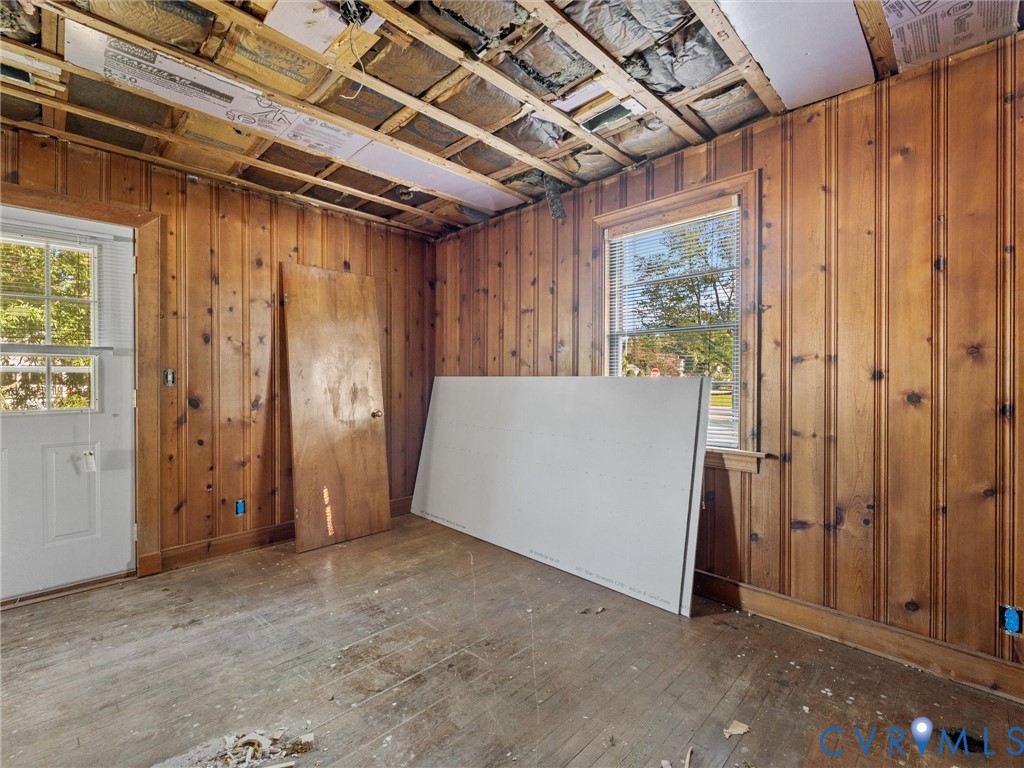 Wood-paneled wall finish, exposed ceiling joists, multi-pane window, and exterior-access door