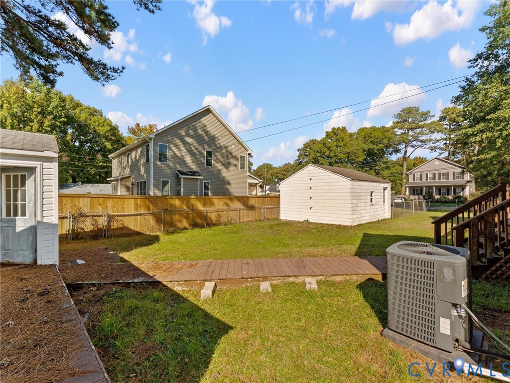 Backyard featuring a wood-plank pathway, detached storage structure, privacy fencing, and mature trees