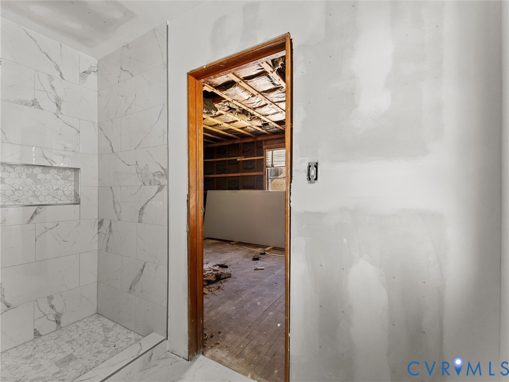 Shower enclosure featuring large-format veined tile walls, hexagonal inset tile niche, and natural wood-finish door casing