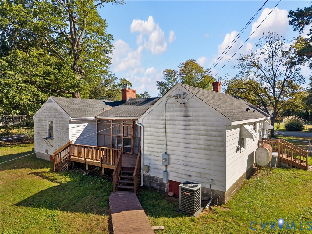 Exterior featuring white siding, a shingled roof with dual brick chimneys, a screened-in porch, wood decking, and a grass-covered lot