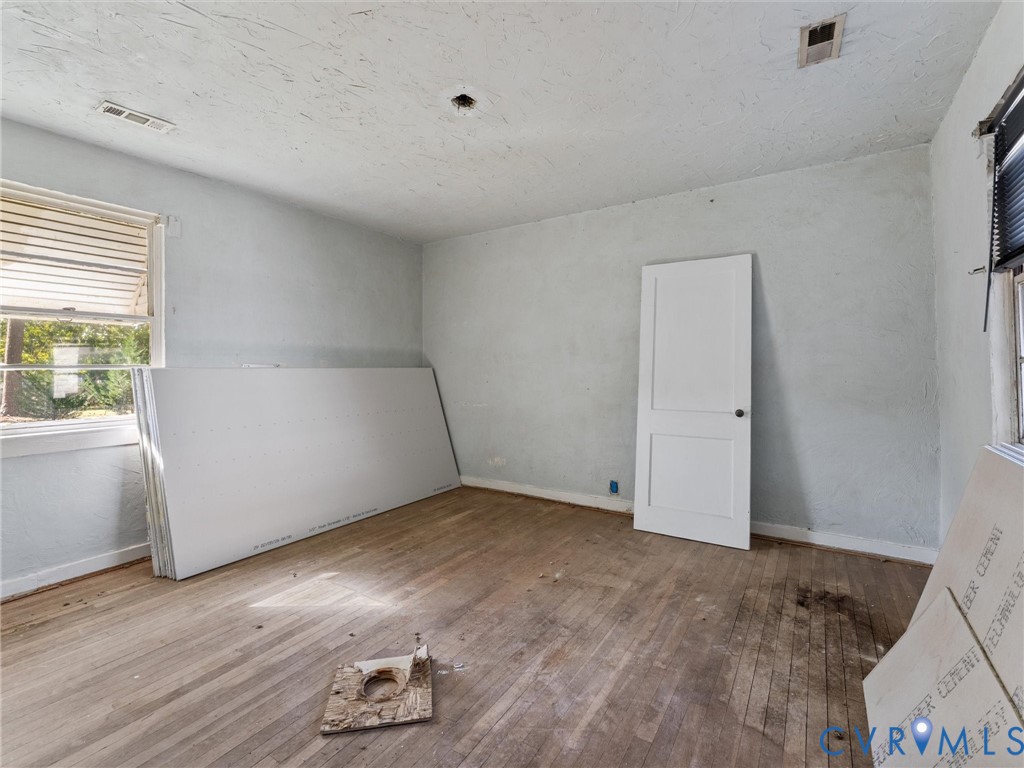 Room interior featuring wood-finish flooring, a two-panel solid core door, and windows with integrated blinds