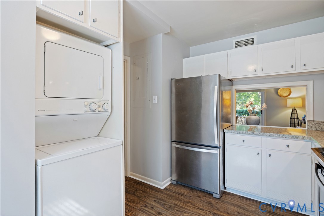 Stacked laundry center with overhead cabinetry, stainless steel bottom-freezer refrigerator, white shaker-style cabinetry, stone-finish countertops, and wood-finish flooring