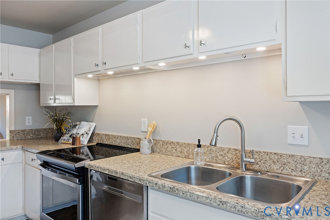 Kitchen featuring white cabinetry, stone-finish countertops, stainless steel dual-basin sink with high-arc faucet, integrated under-cabinet lighting, and stainless steel appliances