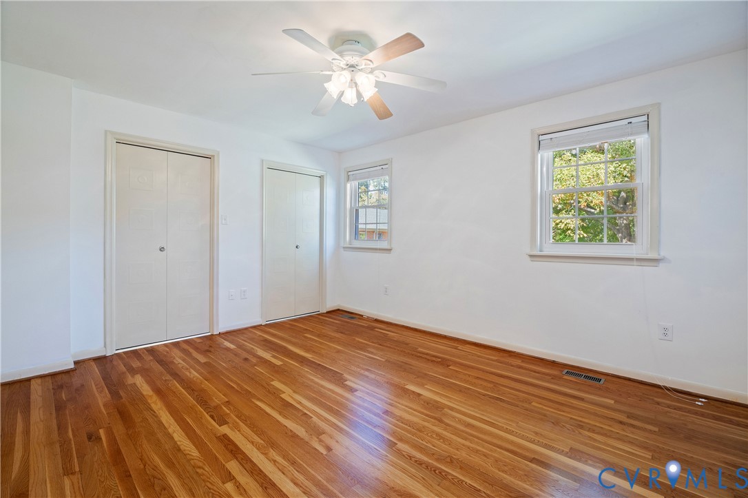 Room featuring wood-finish flooring, dual closets with bi-fold doors, multi-pane windows, and a ceiling-mounted light fixture with fan