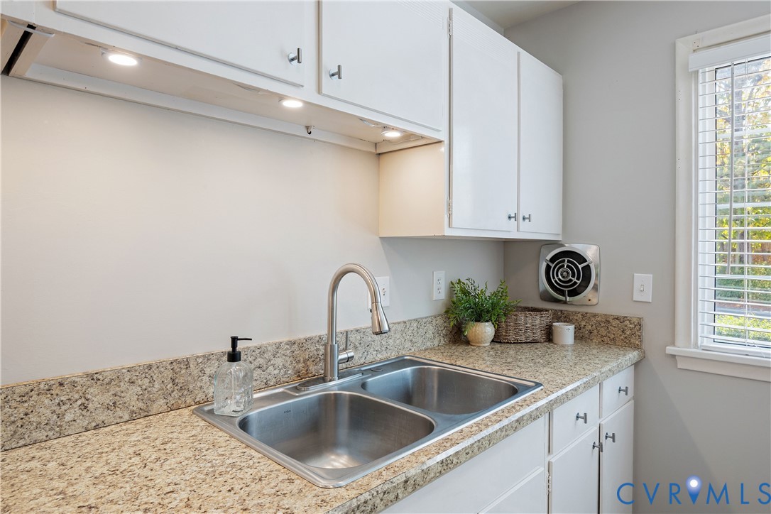 Kitchen area featuring speckled stone countertops, dual-basin stainless steel sink with high-arc faucet, white cabinetry, under-cabinet lighting, and an integrated exhaust fan