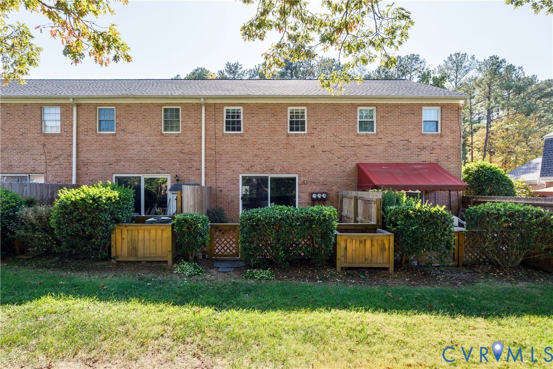 Brick exterior featuring a wood-fenced outdoor space, a retractable fabric awning, and mature shrubbery
