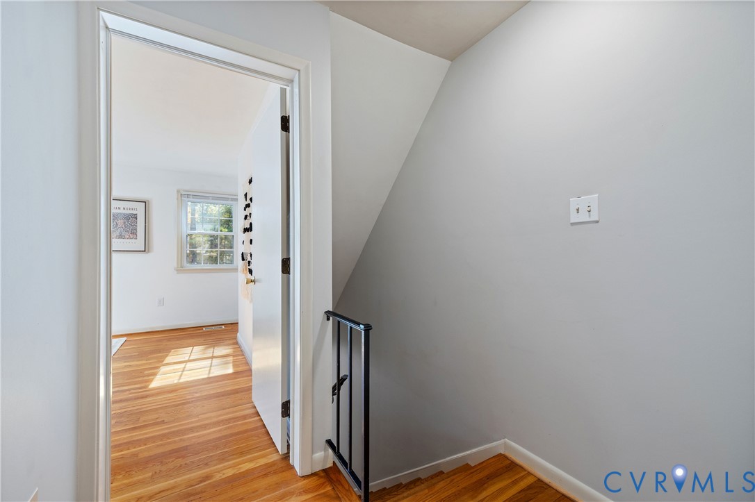 Staircase featuring wood-finish flooring and a black metal handrail, complemented by a white interior door and neutral wall paint
