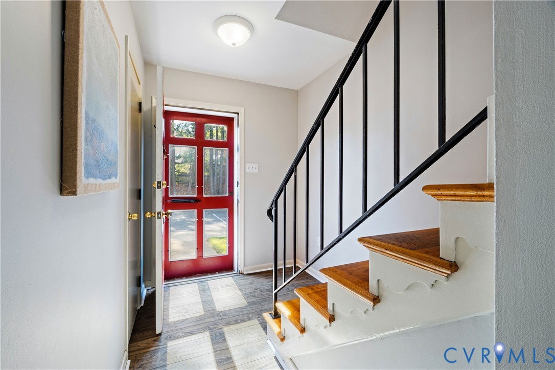 Entryway featuring a red paneled front door with glass inserts, wood-finish flooring, and a staircase with stained wood treads and a black metal railing Entryway featuring a red paneled front door with glass inserts, wood-finish flooring, and a staircase with stained wood treads and a black metal railing