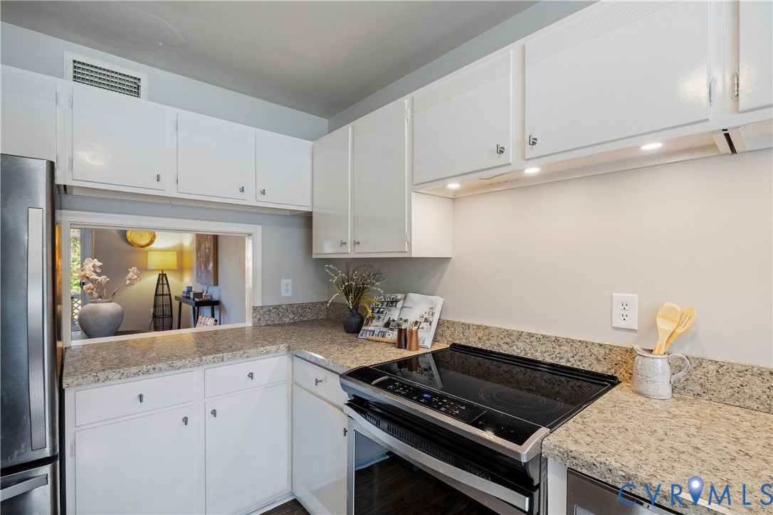 Kitchen featuring white cabinetry, stone-finish countertops, stainless steel appliances, and a pass-through opening