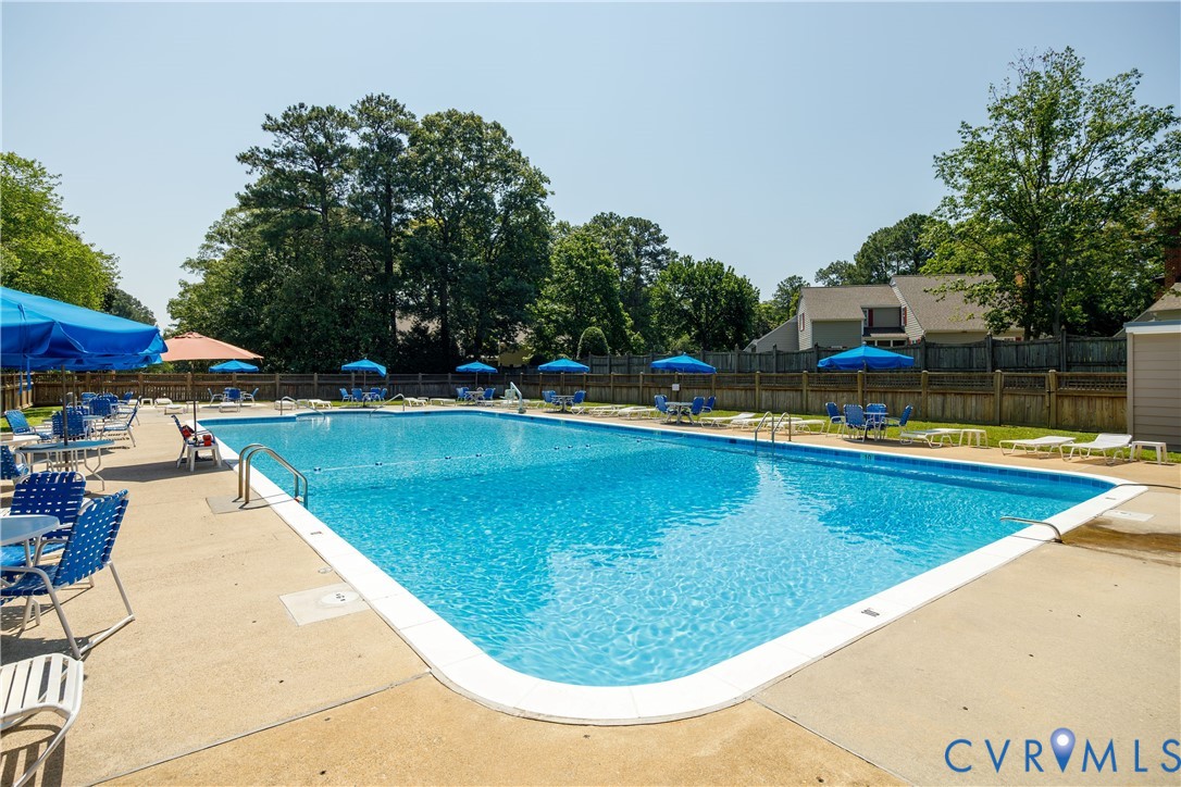Rectangular outdoor swimming pool featuring a concrete deck, metal pool ladder, and perimeter fencing
