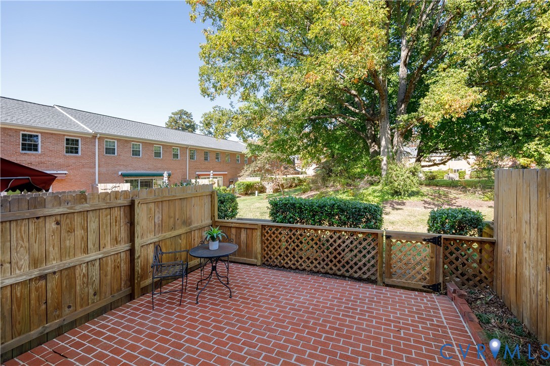 Red brick patio featuring a wood privacy fence, lattice detailing, and a gated entrance