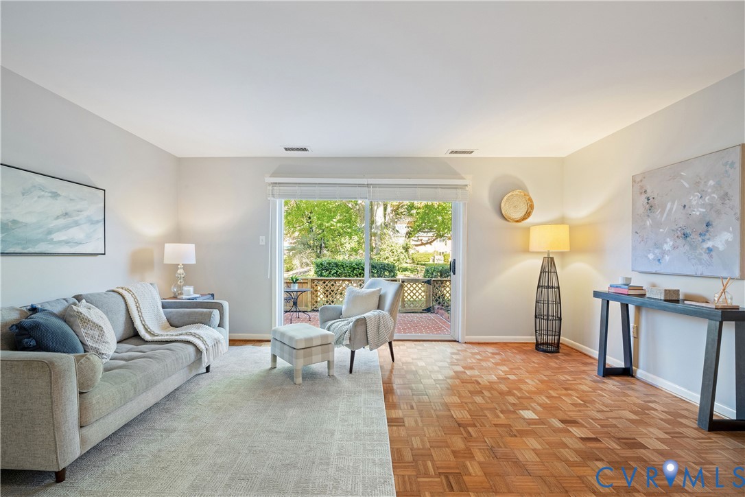 Living area featuring parquet wood-finish flooring and large sliding glass doors opening to a brick patio Living area featuring parquet wood-finish flooring and large sliding glass doors opening to a brick patio