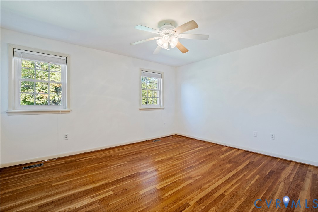 Interior room featuring wood-finish flooring, two multi-pane windows with trim, and a ceiling fan with integrated lighting