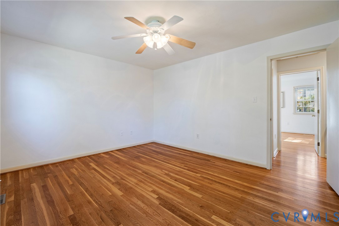 Room featuring wood-finish flooring, white walls, and a ceiling-mounted light fixture with a fan