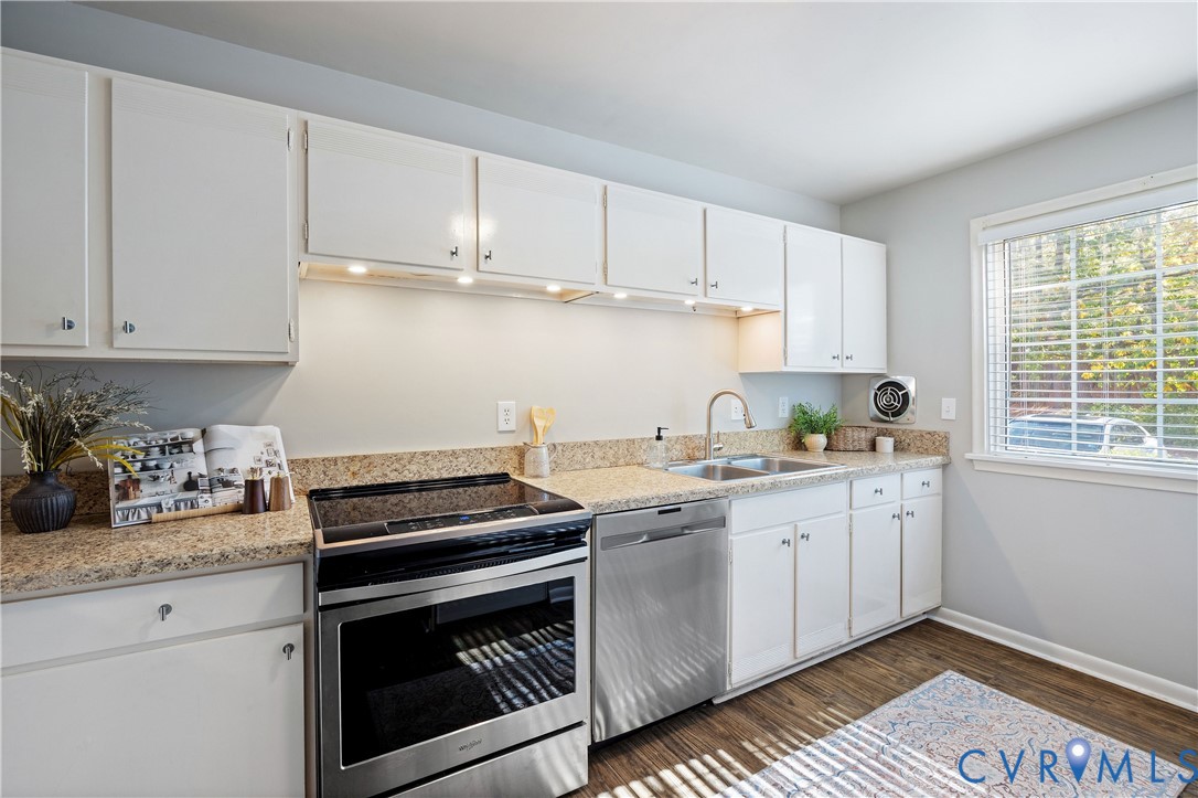 Kitchen featuring white cabinetry, stone-surface countertops, stainless steel appliances, under-cabinet lighting, and wood-finish flooring
