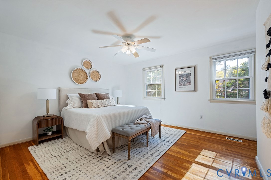 Bedroom featuring wood-finish flooring, dual windows with natural light, and a ceiling-mounted light fixture with a fan