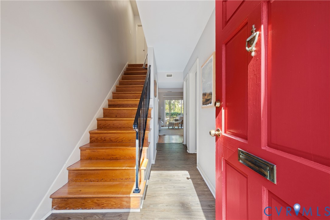 Entryway featuring a bold red paneled front door, wood-finish staircase with metal balusters, and wood-finish flooring Entryway featuring a bold red paneled front door, wood-finish staircase with metal balusters, and wood-finish flooring