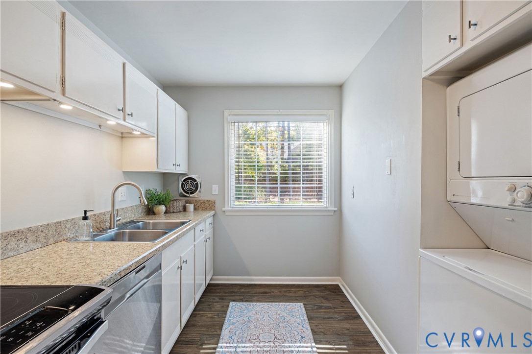 Utility room featuring white cabinetry, stone-finish countertops, stainless steel dual-basin sink, wood-finish flooring, and stacked laundry unit