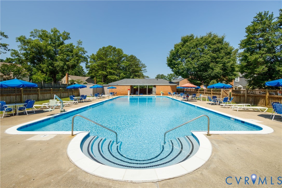 Rectangular outdoor swimming pool featuring a curved walk-in staircase with stainless steel handrails, concrete decking, and a brick-facade pool house