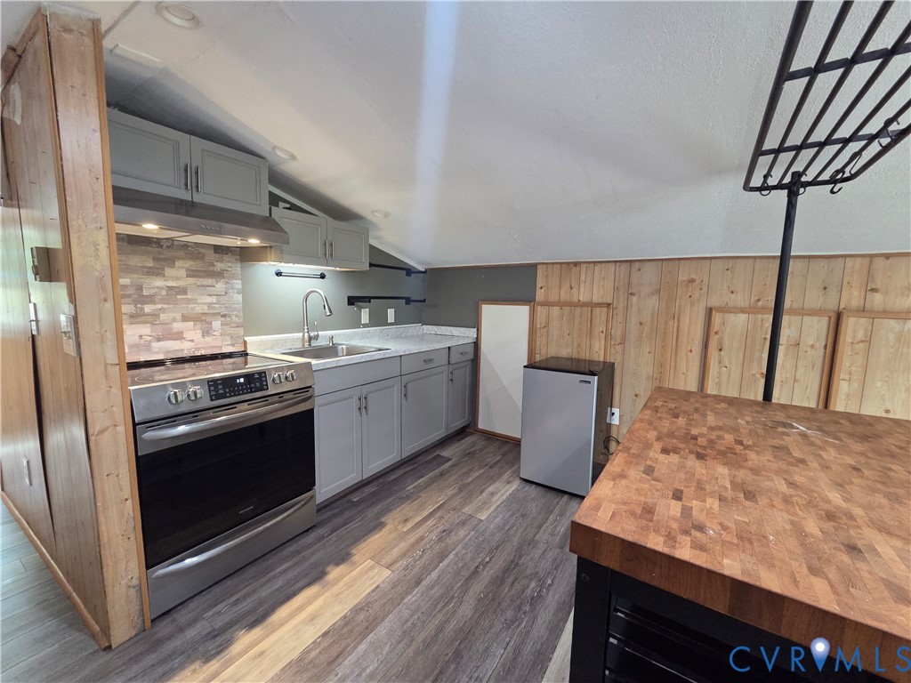 Kitchen featuring light gray cabinetry, stainless steel range, stone-tiled backsplash, butcher-block countertop, and wood-finish flooring