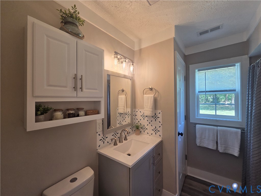 Bathroom vanity featuring a quartz-finish countertop, undermount sink, patterned tile backsplash, white wall-mounted storage cabinetry, and brushed nickel hardware