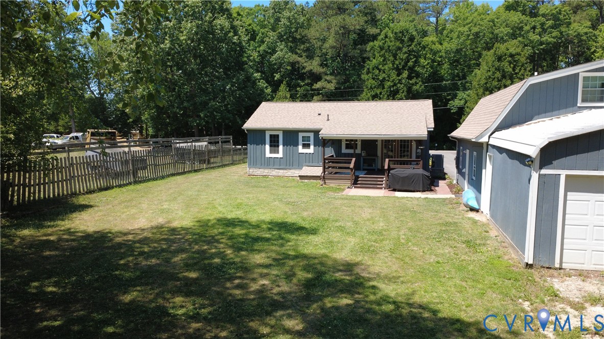 Rear exterior featuring vertical siding, a wood deck with stairs, a paved patio area, an attached garage structure, and a fenced backyard